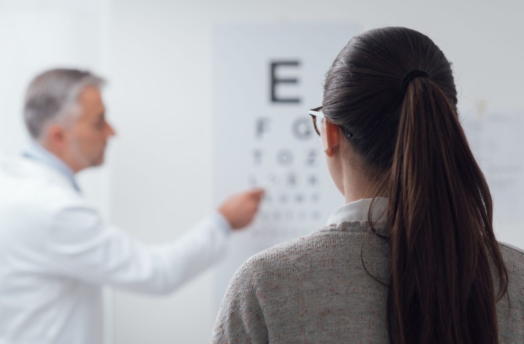 View from behind a woman's head as she looks ahead at her eye doctor pointing to an eye chart.