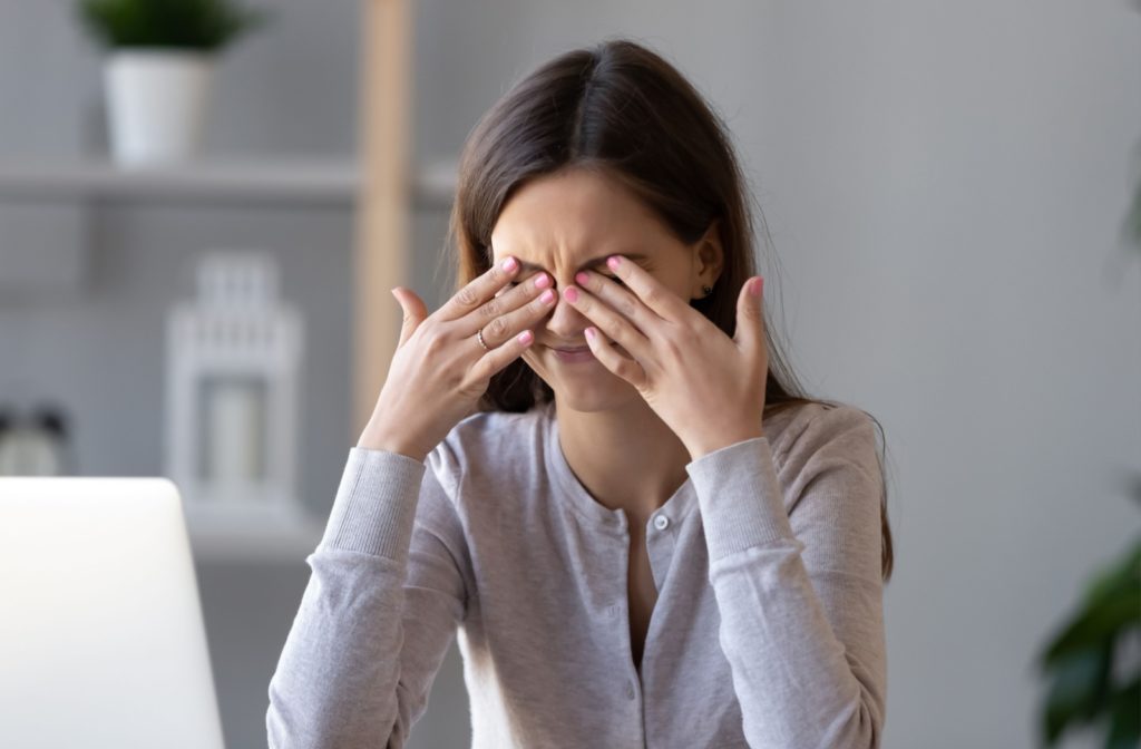 A woman sitting in front of a computer rubbing her eyes due to irritation from dry eyes