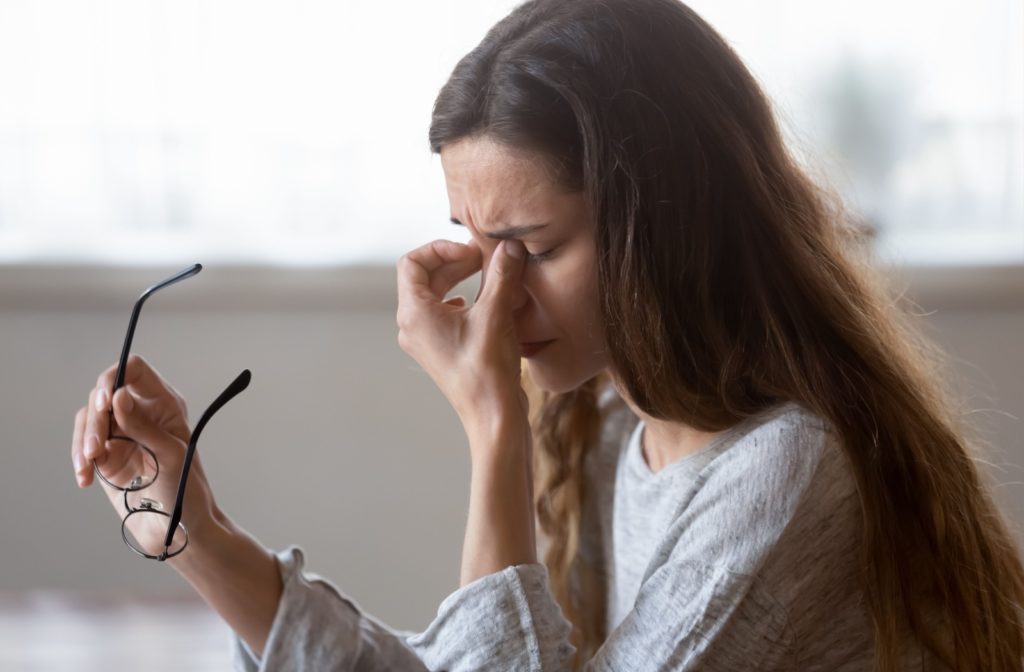 A young woman taking off her glasses and rubbing her eyes due to dry eye discomfort.