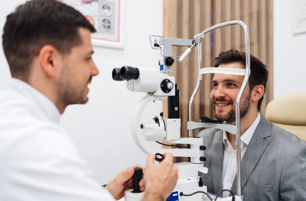 An optometrist talks to their patient during an eye exam using a slit lamp.