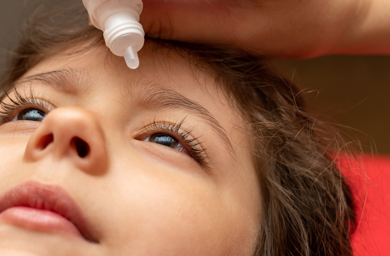 A close-up image of a child lying down while their out-of-frame parent applies eye drops to their left eye.
