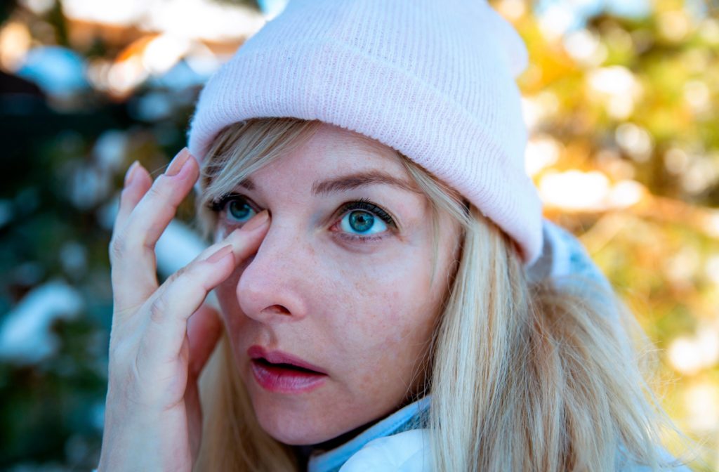 An image of a person outdoors in the cold scratching their dry eyes that are irritated from the cold weather.