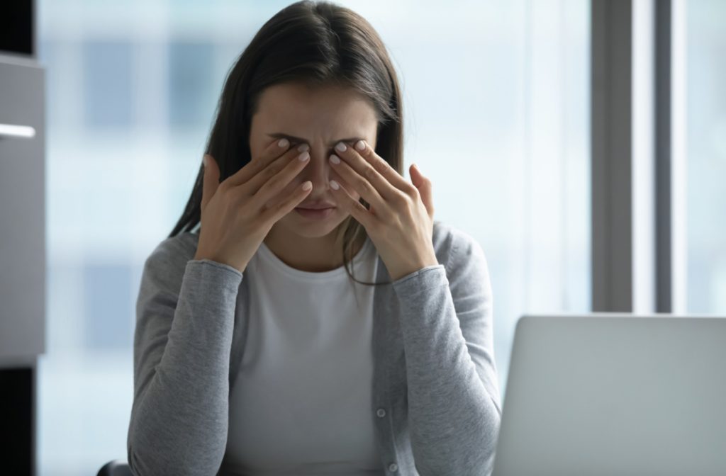 A young adult working at their computer and rubbing their eyes in frustration due to discomfort from dry eyes.