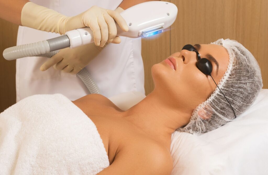 Person wearing eye protection receives IPL therapy on face from a gloved professional using handheld device