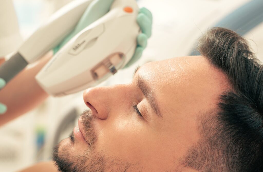 Person lies still with eyes closed as technician applies IPL treatment near lower eyelid using a light-based device