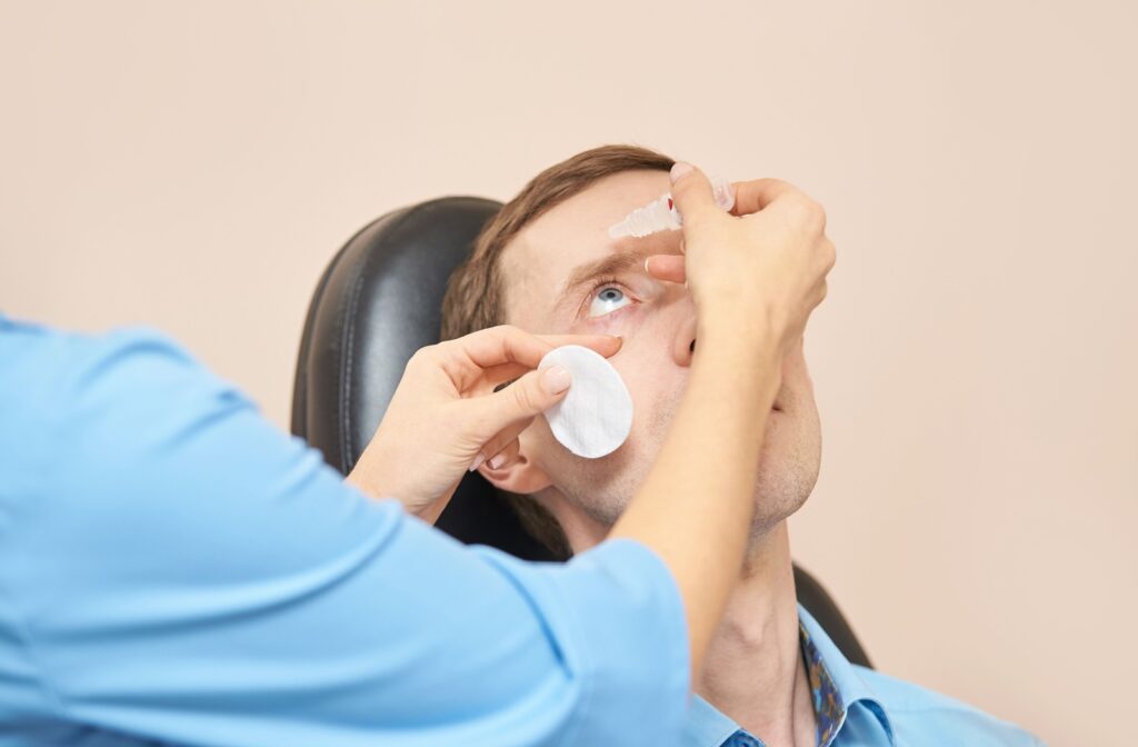 Person receiving lubricating eye drops during eye exam while holding a cotton pad under eye
