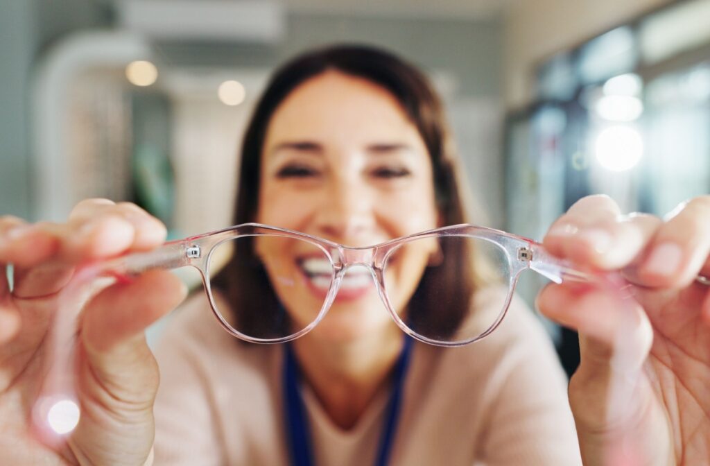 An optician holds a pair of pink glasses up in front of them ready to fit them on a patient