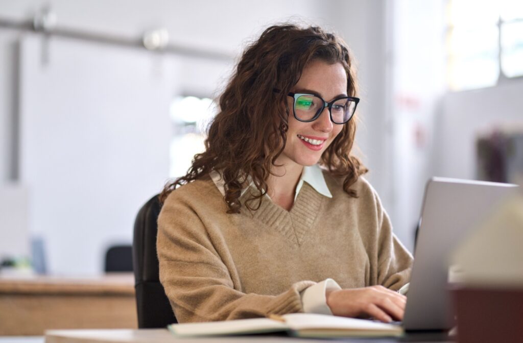 A person wearing glasses is smiling while they work on a computer
