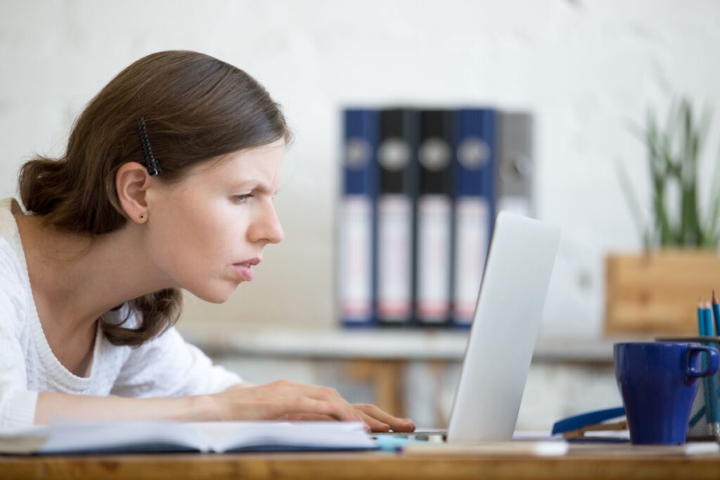 A person sitting really close to their laptop and squinting in order to see the screen better